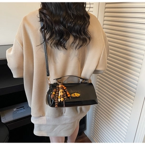 Détail d'un sac bandoulière noir brillant avec fermoir doré et pendentif en perles