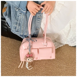 Pink glossy Boston bag with front pockets and charm shown in handheld use