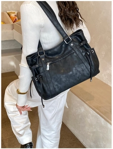 Detailed view of a black leather tote bag with silver zippers and drawstring side pockets