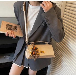 Détail du sac bandoulière beige avec fermoir doré et pendentif en perles de bois