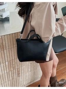 Close-up of minimalist black underarm bag with half-moon design and detachable metal strap