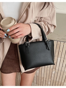 Close-up of black lychee grain texture and silver metal buckle on leather handbag