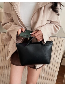 Detail shot of a black leather handbag with a fine texture and soft sheen held by a model