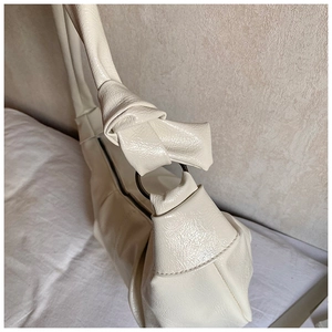 Close-up of cream pleated leather texture and metal knot hardware on a shoulder bag