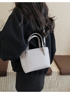 Detail of beige lychee grain leather handbag featuring metal buckle and slim shoulder strap