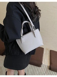 Detail of light grey basket bag showing pebbled leather texture and metal buckle accents