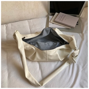 Detail view of cream leather tote bag featuring striped lining and shoulder strap knot