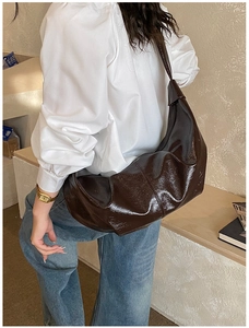Deep brown high-gloss crescent hobo bag featuring pleated texture on a casual model outfit
