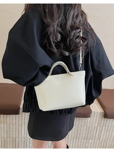 Minimalist beige crossbody bag styled on shoulder over oversized black coat