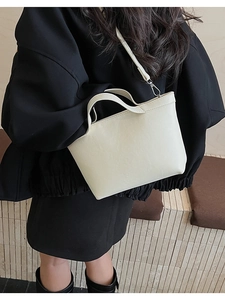 Close-up of creamy white trapezoid handbag with litchi grain texture and silver hardware