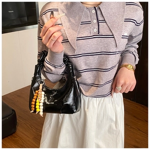 Detail of black patent leather dumpling bag with pleated handle and colorful bead charm