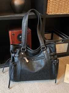 Large black vintage tote bag with functional pockets and silver hardware on a wooden shelf