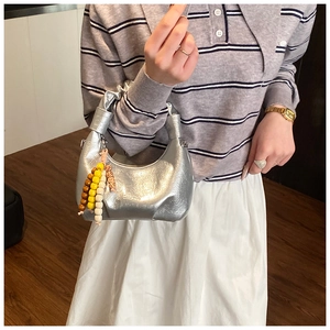 Details einer silbernen Hobo-Tasche mit Lederfalten und buntem Perlen-Quasten-Anhänger