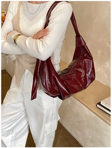 Close-up of a glossy burgundy pleated hobo bag with knotted strap details and shiny finish