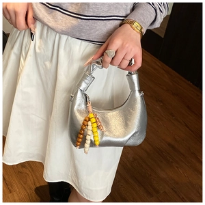 Detail of silver metallic hobo bag with knotted handle and colorful bead charm accessory