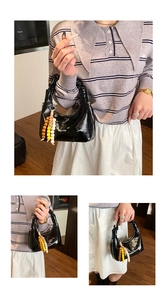 Detail of black patent leather crescent bag with pleated handle and colorful bead charm