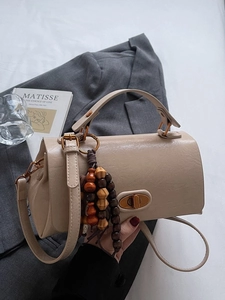 Sac à main kaki chic avec gland en perles de bois posé sur un blazer gris