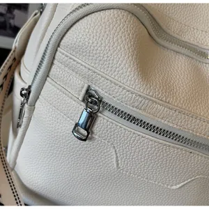 Close-up of smooth silver zipper and lychee grain texture on cream fashion backpack