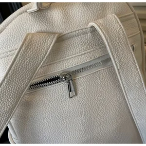 Detail of white lychee grain leather backpack featuring smooth silver metal zippers