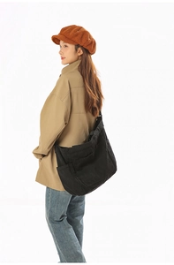 Side view of large black canvas messenger bag showing multiple storage pockets on a model