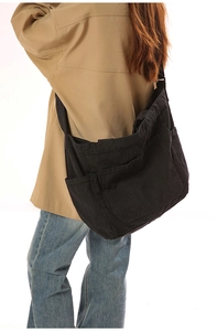 Detail showing spacious black canvas messenger bag with functional side pockets on model
