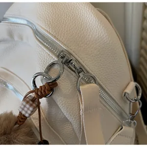 Detail of silver ring zipper on white pebble leather backpack with a decorative pompom charm