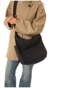 Close-up of a black canvas crossbody bag with functional pockets worn by a model