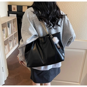 Detail of black leather tote bag with gold chain strap and fluffy white charm on side