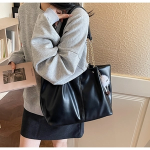 Fashionable black leather tote bag with gold chain strap and fluffy eye charm detail
