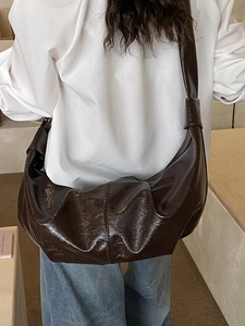 Dark brown high-gloss leather hobo bag with wide shoulder strap worn by female model