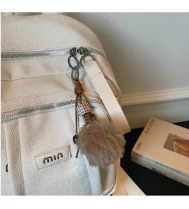 Détail du sac à dos blanc cassé texture litchi avec logo argenté et pompon brun