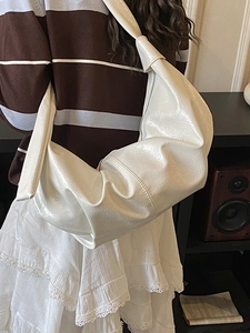 Glossy white patent leather hobo bag with knotted shoulder strap worn by a model