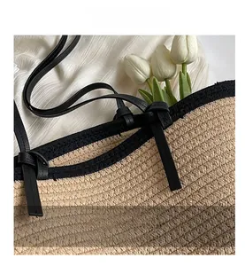 Close-up of black leather straps knotted to the beige woven straw tote bag surface