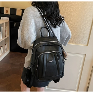 Détail d'un sac à dos en similicuir noir avec bandoulières géométriques et pompon rose