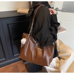 Detail of large brown tote bag with gold chain strap and plush pendant on model
