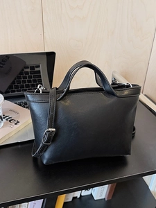 Minimalist black trapezoid shoulder bag with dual handles and adjustable silver strap