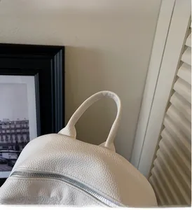 Detail of white leather backpack showing top handle and silver metal zipper closure