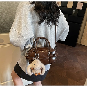 Close-up of brown glossy shoulder bag with a plush bunny charm on a lifestyle model