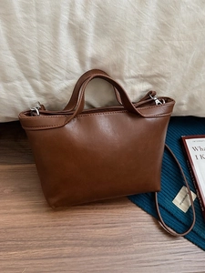 Classic brown leather tote bag on wooden floor with shoulder strap for daily commuting