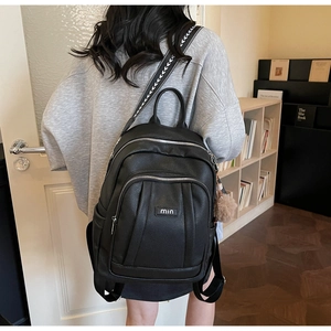 Détail d'un sac à dos en cuir noir avec sangle ondulée et pompon marron doux