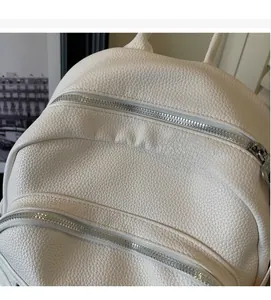 Close-up of off-white lychee texture leather with dual silver zippers on backpack