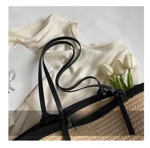 Detail of straw woven tote bag featuring black shoulder straps and knotted handle design