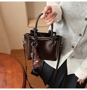 Detalle del bolso de cubo en cuero encerado marrón oscuro con asa anudada y colgante de oso
