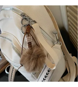 Close-up of white lychee texture backpack with silver zippers and plush brown ball charm