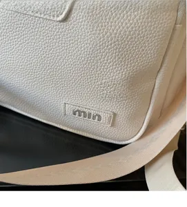 Detail of white lychee grain leather backpack with silver metal min logo and woven strap