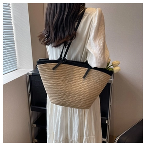 Detail of straw woven tote bag with black contrast trim and leather shoulder strap worn by model
