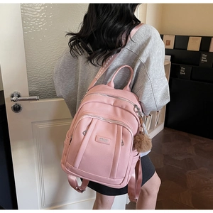 Détail du sac à dos rose en cuir grainé avec logo, pompon et bandoulière imprimée