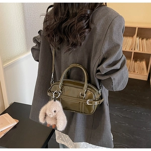 Detail of dark olive green leather Boston bag with plush bunny charm in a cozy setting