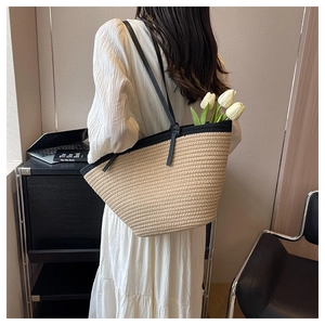 Detailed back view of a large straw tote bag with black contrast straps on a person