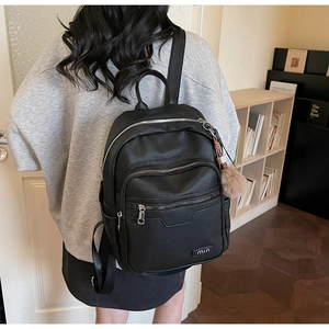 Detail of black pebbled leather backpack with multi-zipper layers and plush ball charm